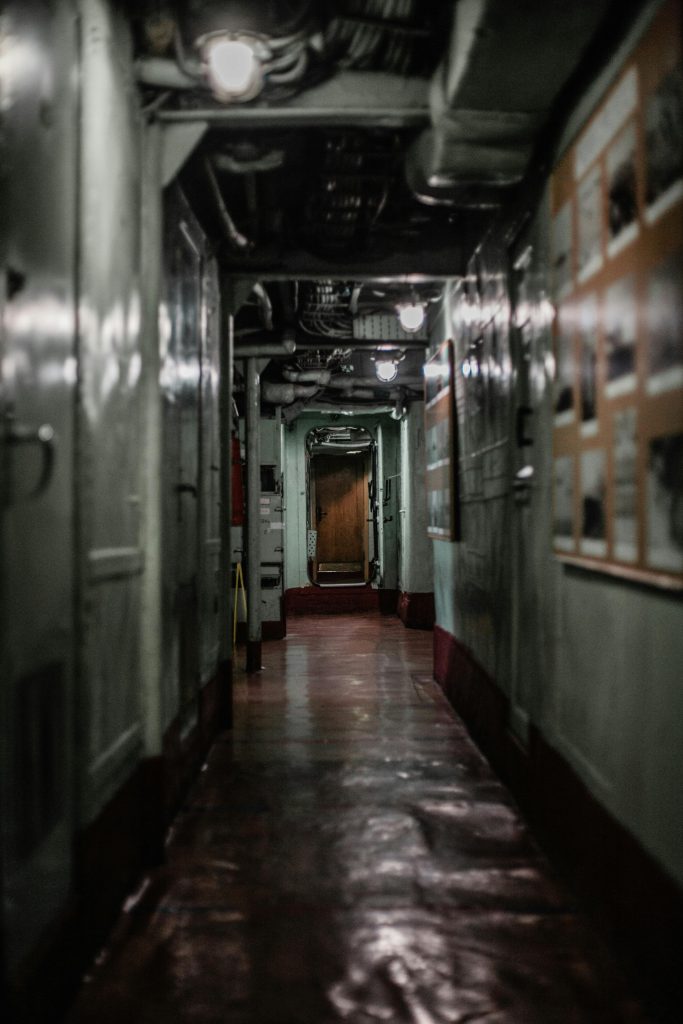 Dark and moody interior hallway of an industrial ship, showcasing pipes and worn details.